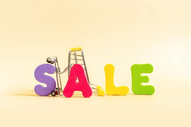 Word SALE written in bright colorful letters and Shopping cart isolated on pastel background.