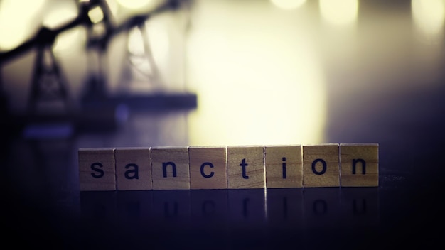 Word sanctions spelled in letters on table made of wooden block letters with dramatic lighting and smoke