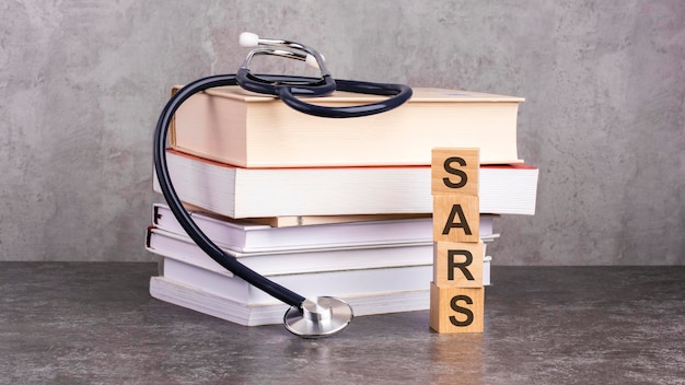 Word sarsは、聴診器の近くの木製の立方体に、灰色の背景の病院クリニックの医療概念と、本と聴診器を使用した医学教育の医療ビジネス概念に書かれています。