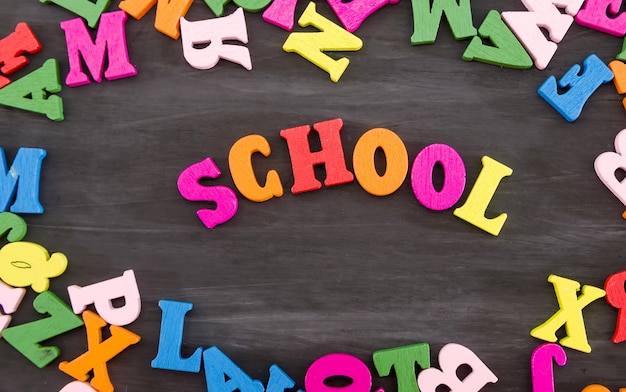 黒い木製の背景に色付きの文字で作られた単語学校