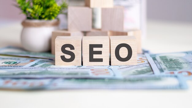 Word SEO is geschreven op houten kubussen. de kubussen bevinden zich op de bankbiljetten die op tafel liggen. op de achtergrond een groene plant in een pot. SEO - afkorting van zoekmachine optimalisatie