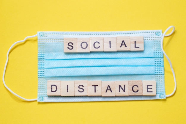 Word Social Distance made from wooden letters on blue medical mask.