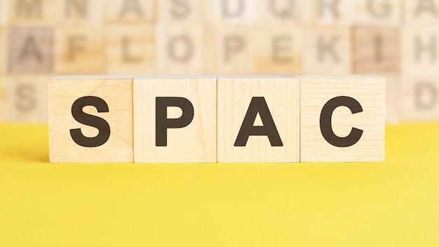 The word spac is written on wooden cubes on a bright yellow surface. in the background are rows of cubes with different letters. business and finance concept