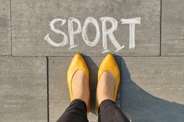 Word sport written on gray pavement with woman legs