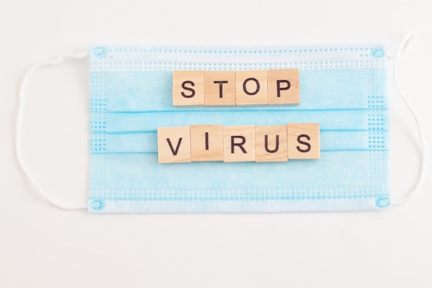 Word STOP Virus made from wooden letters on blue medical mask.