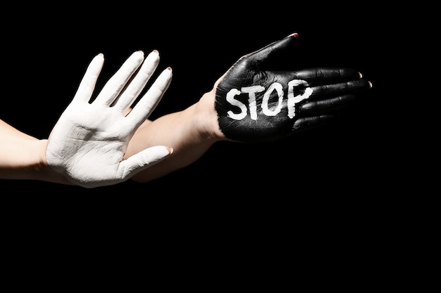 Photo word stop written on painted female palm against dark background. racism concept