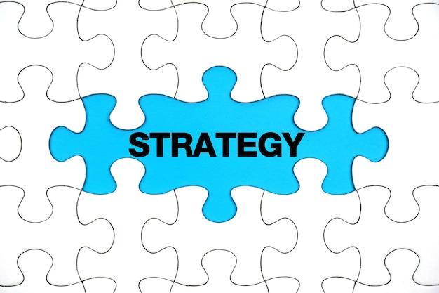 The word STRATEGY on the blanks of the White jigsaw puzzle on blue background