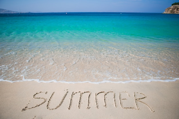 Photo word summer handwritten on sandy beach with soft ocean wave on background