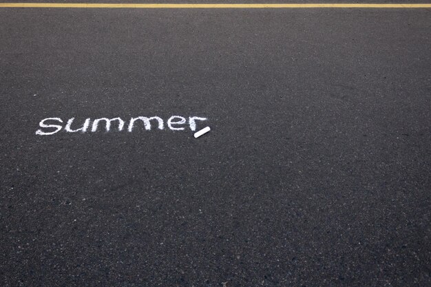 The word summer written on black asphalt with white chalk with a yellow road marking line