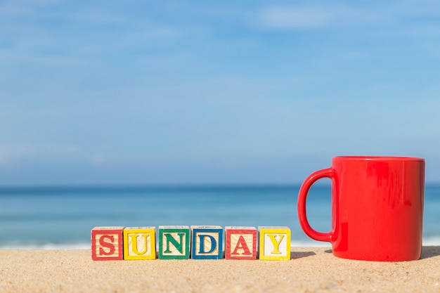 Photo word sunday in colorful alphabet blocks and coffee cup on tropical beach, phuket thailand