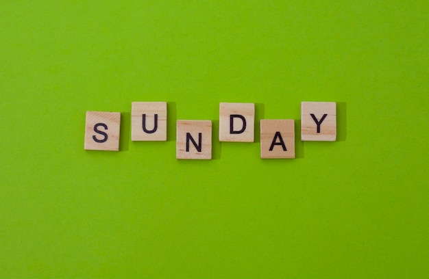 The word sunday. text day of the week in wooden letters.black letters on a tree, light green