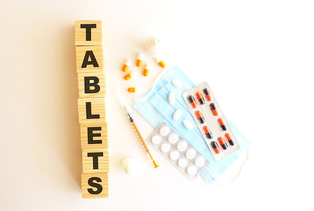 The word TABLETS is made of wooden cubes on a white background with medical drugs and medical mask.