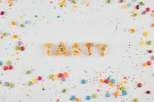 Photo word tasty made of homemade cookies on light grey background witgh sweet rainbow sprinkles