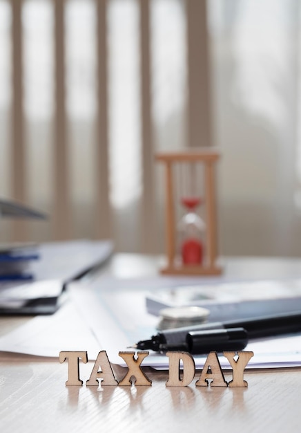 Photo word tax day composed of wooden letters. coins, papers, pen in the background. closeup