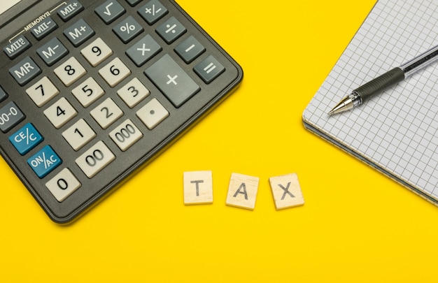 Word tax made with wood letters on yellow and modern calculator with pen and notebook.