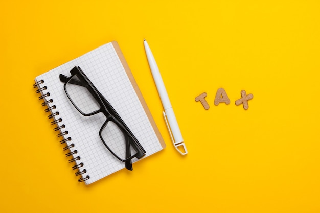 Word tax and notebook with glasses on yellow