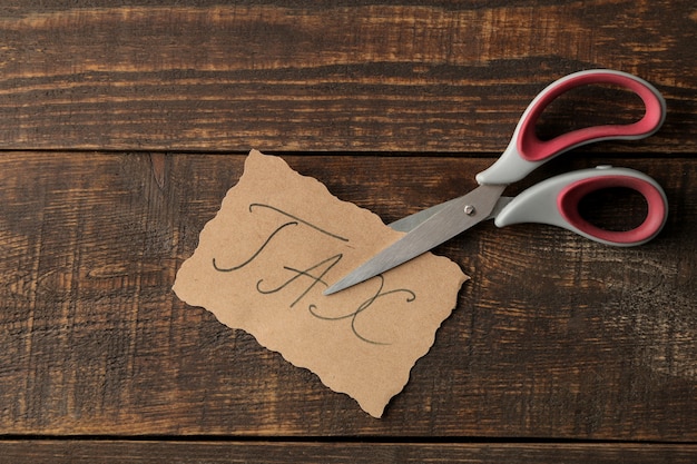 Word tax with scissors on a brown wooden background. view from\
above