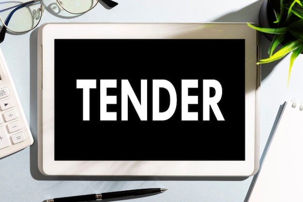 사진 태블릿, 계산기, 안경, 노트북, 사무실 책상 위의 펜에 있는 단어 tender. 비즈니스 개념입니다.