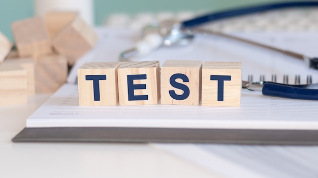 The word Test is written on wooden cubes near a stethoscope on a paper wall. Medical concept.