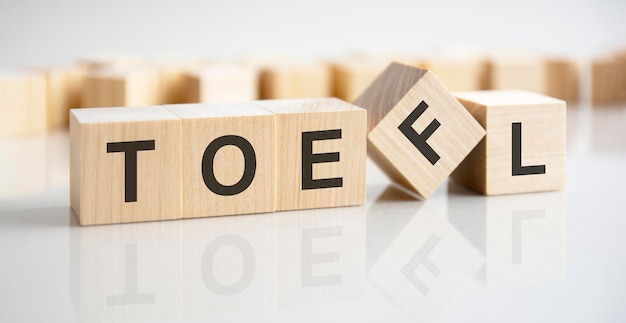 白い背景の上の木製の立方体に書かれた TOEFL という言葉