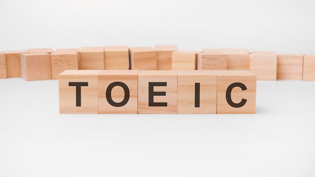 Word TOEIC은 테이블과 밝은 배경에 놓인 나무 빌딩 블록으로 만들어졌습니다. 개념. TOEIC - Test of English for International Communication의 줄임말