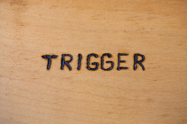 The word trigger handwritten on flat bare plywood surface with woodburner