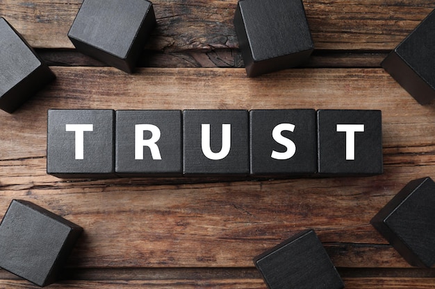 Word TRUST made with black cubes on wooden table flat lay