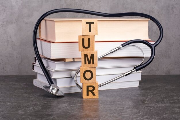 The word TUMOR is written on wooden cubes near a stethoscope on a paper background concept of medical education with book and stethoscope