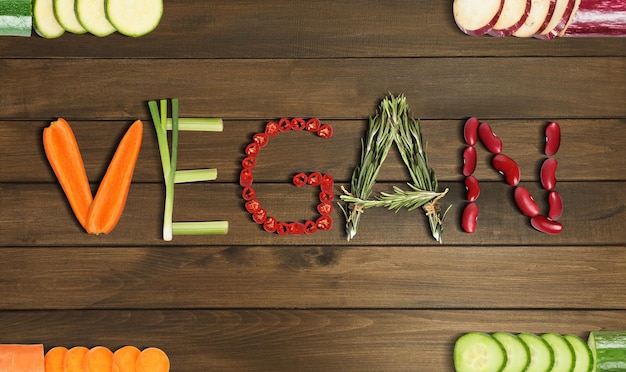 Фото Слово vegan из различных свежих вкусных овощей на деревянном фоне плоской планировки