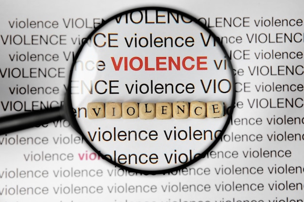 Word VIOLENCE made of wooden cubes under magnifying glass on white background top view