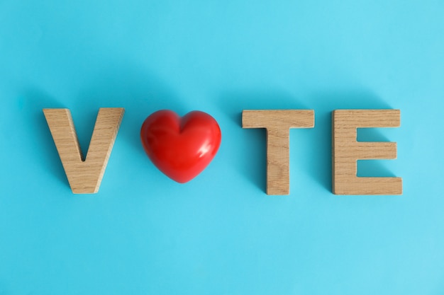 Word Vote made of wooden letters and heart on blue surface