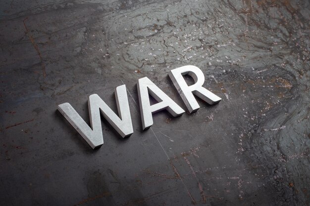 Слово " война " написано серебряными металлическими буквами на черной поверхности из необработанной стали в диагональной перспективе.