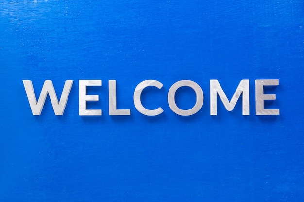 The word welcome laid with silver metal characters on blue painted wooden board in flat lay with central composition