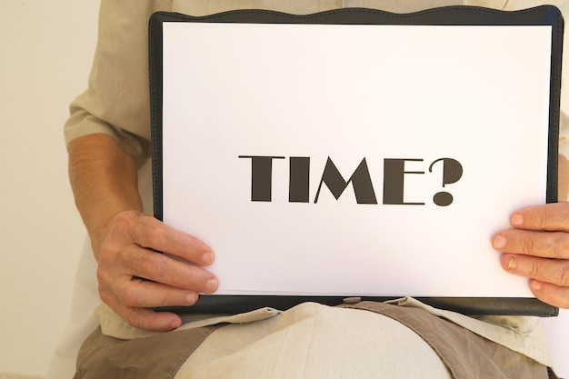 A word on a white paper in the hands of senior woman: "Time?"