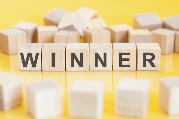 Photo the word winner is written on a wooden cubes structure. blocks on a bright yellow background. financial concept. selective focus. toy blocks around.