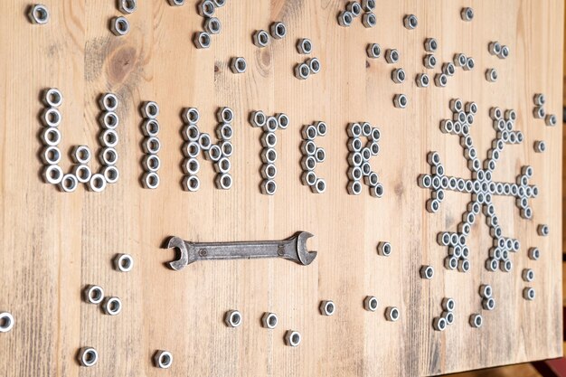 La parola inverno e un fiocco di neve sono rivestiti con dadi di metallo su un tavolo di legno accanto a una chiave inglese