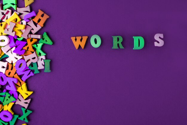 Word word made with block wooden letters next to a pile of other letters over the wooden board surface composition