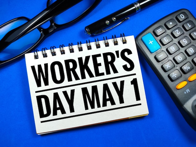 Word WORKER'S DAY MAY 1 on blue background with calculatorpen and glassesLabour day concept