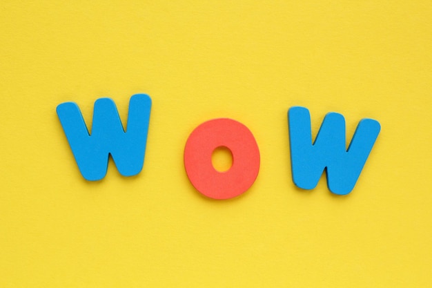 Word WOW colored letters on yellow background. Positive, happy, fun concept. Flatlay, top view
