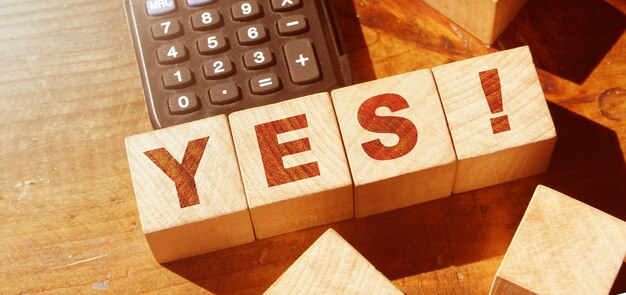 Слово "да" на деревянных блоках и калькуляторе Бизнес-мотивация и концепция образования