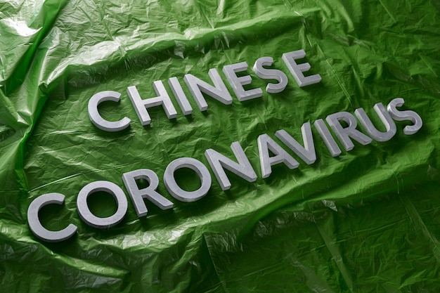 緑のしわくちゃのプラスチックフィルムの斜めの構成に銀の金属の文字で置かれた単語中国のコロナウイルス