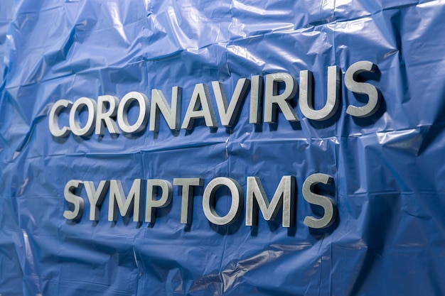 코로나바이러스 증상이라는 단어는 구겨진 파란색 플라스틱 필름 선형 원근 구성에 은색 문자로 표시되며 선택적 초점