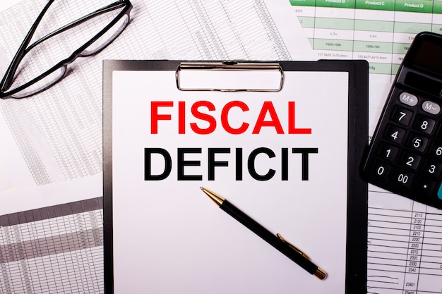 FISCAL DEFICITという言葉は、眼鏡と電卓の近くの白い紙に書かれています。