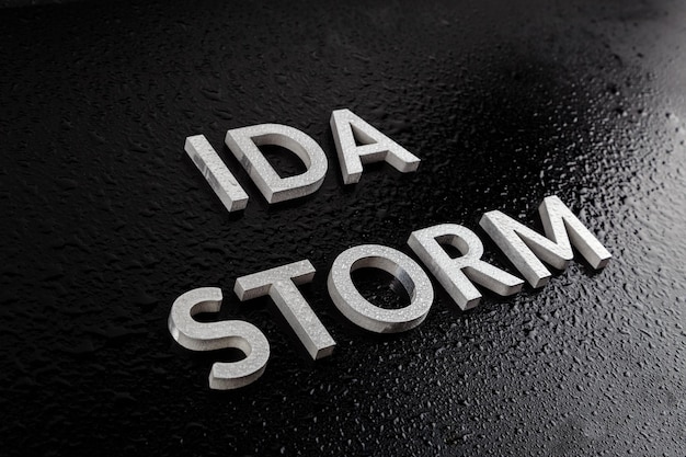 Слова ida storm, выложенные серебряными металлическими буквами на черной поверхности, покрытые каплями дождевой воды