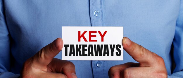 The words KEY TAKEAWAYS is written on a white business card in a man's hands. Business concept