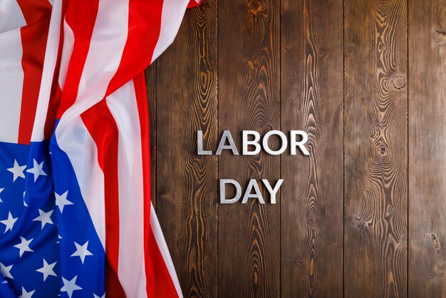 Words labor day laid with silver metal letters on wooden surface with crumpled usa flag on left side