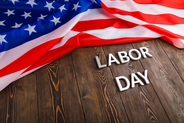 Words labor day laid with silver metal letters on wooden surface with crumpled USA flag on left side