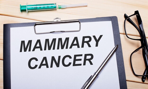 MAMMARY CANCER이라는 단어는 검은 색 테두리가있는 안경, 펜 및 주사기 옆의 흰색 종이에 쓰여 있습니다.