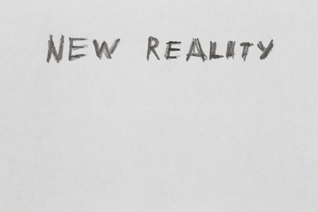 The words new reality handwritten on blank white paper with pencil