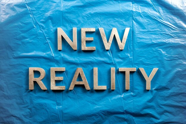 The words new reality laid with white letters over crumpled blue plastic film background